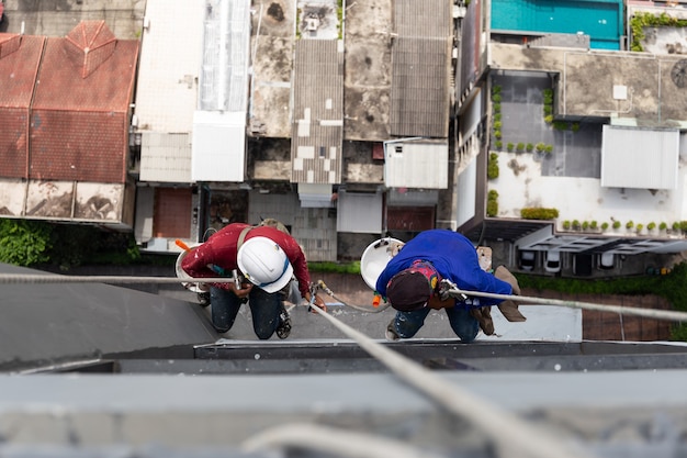 Pintores asiáticos colgando de la cuerda de color de pintura en la pared del edificio