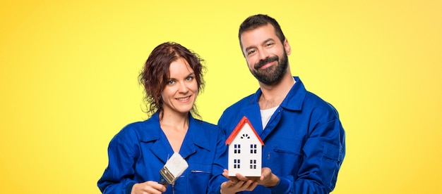 Foto pintores que sostienen una pequeña casa en fondo colorido