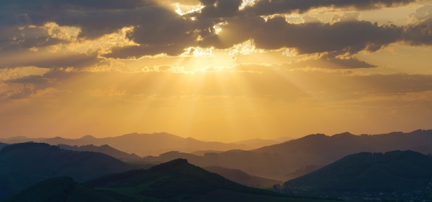 Pintoresco amanecer en las montañas, rayos de sol a través de las nubes