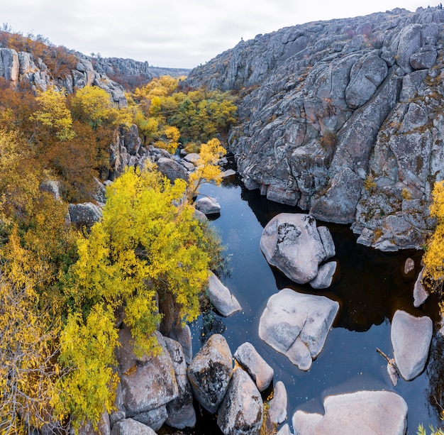 Un pintoresco arroyo fluye en el cañón de Aktovsky rodeado de árboles otoñales y grandes rocas de piedra