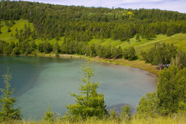 Un pintoresco lago rodeado de montañas con césped verde y árboles.