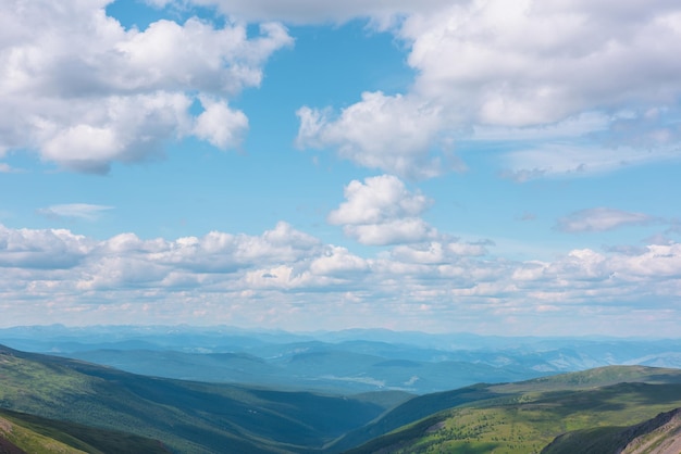 Pintoresco paisaje aéreo con la inmensidad de la montaña verde bajo nubes cúmulos en el cielo azul en un clima cambiante Vista superior impresionante y colorida al valle del bosque entre colinas iluminadas por el sol y montañas en el horizonte