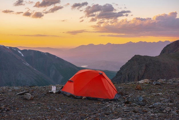 Pintoresco paisaje alpino con carpa a gran altura con vista a grandes montañas en el cielo naranja del amanecer Carpa naranja vívida con vista impresionante a la alta cordillera bajo el cielo nublado en colores del atardecer