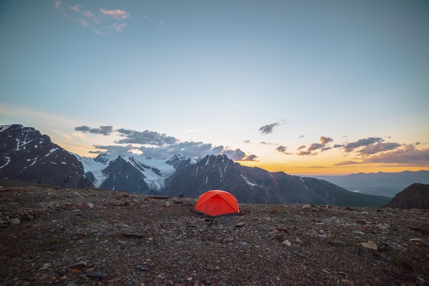 Pintoresco paisaje alpino con carpa a gran altura con vista a grandes montañas en el cielo naranja del amanecer Carpa naranja vívida con vista impresionante a la alta cordillera bajo el cielo nublado en colores del atardecer