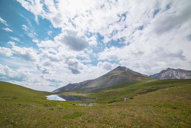 Pintoresco paisaje alpino con un pequeño lago en un valle de montaña verde iluminado por el sol bajo un cielo nublado Espectacular paisaje soleado con un pequeño lago de montaña y una alta montaña rocosa bajo las nubes en un clima cambiante