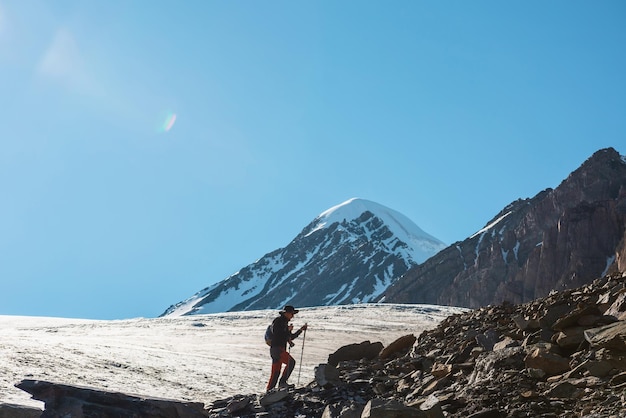 Pintoresco paisaje alpino con silueta de excursionista con bastones de trekking contra una gran lengua glaciar y pico de montaña nevada a la luz del sol Hombre con mochila en altas montañas bajo un cielo azul en un día soleado