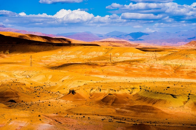 Pintoresco paisaje con dunas de arena naranja y montañas en el desierto del Sahara con cielo azul brillante y nubes en Marruecos