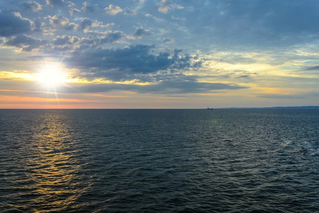 Pintoresco paisaje marino el sol sale sobre el mar contra un cielo nublado y en la distancia se puede ver el barco y la tierra