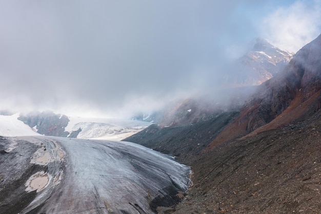 Pintoresco paisaje de montaña con un gran glaciar en nubes bajas en los colores del amanecer Vista colorida a la lengua del glaciar en la luz del sol de la mañana en nubes bajas Paisaje atmosférico de alta montaña temprano en la mañana