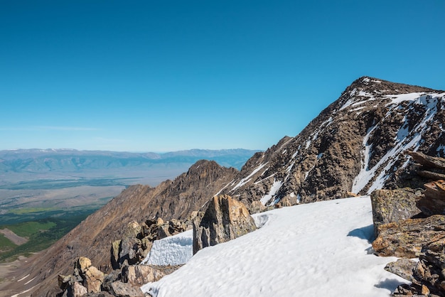 Pintoresco paisaje montañoso con rocas afiladas entre la nieve cerca del abismo a gran altura Impresionante vista de vértigo desde el borde del precipicio con cornisa de nieve hasta una gran cordillera bajo el cielo azul en un día soleado