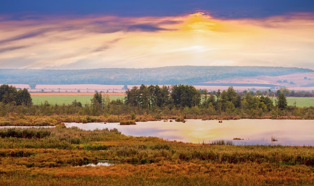 Pintoresco paisaje otoñal con río y árboles durante la puesta de sol.