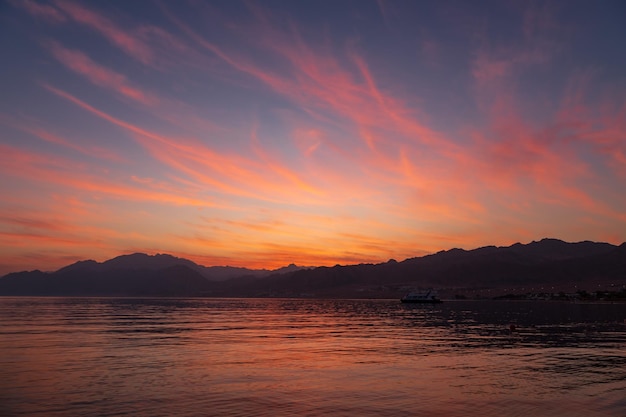 Pintoresco paisaje de puesta de sol en la playa con nubes coloridas y montañas en el fondo Dahab Egipto