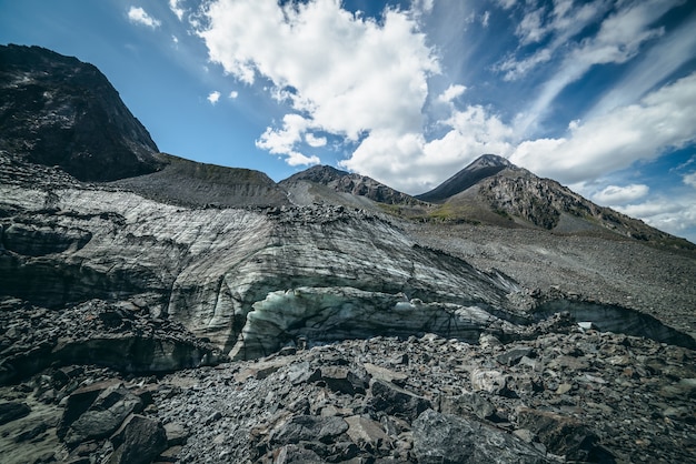 Pintoresco paisaje de las tierras altas con un gran glaciar y la cima de una montaña alta en forma de pirámide en un día soleado. Impresionante paisaje de montaña con colina helada con grandes piedras y pináculo. Hielo de glaciar y piedras a la luz del sol