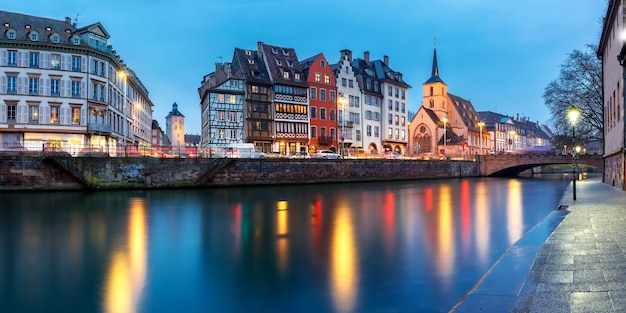 Pintoresco panorama del muelle y la iglesia de San Nicolás con reflejos de espejo en el río Ile durante la hora azul de la tarde, Estrasburgo, Alsacia, Francia