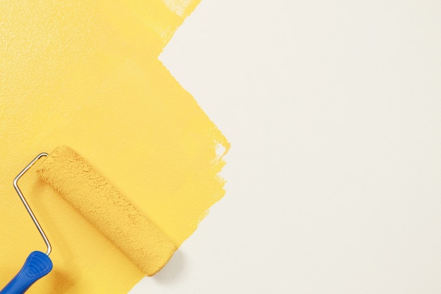 Pintura com escova de rolo, pintura do trabalhador na superfície pintura do apartamento, reformando com tinta de cor amarela.