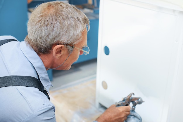 Pintura de produtos metálicos Um idoso pinta um armário com compressor