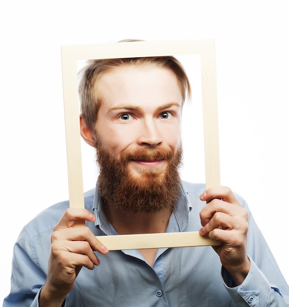 Foto pintura divertida joven con barba sosteniendo el marco de la imagen delante de su cara y divertido hamming aislado en blanco