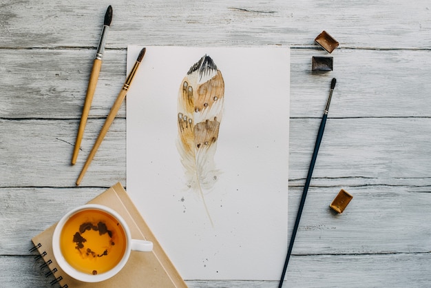 Pintura em aquarela com pincel e caneca de chá na textura de madeira.