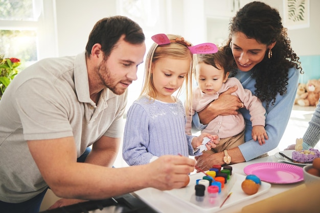 Pintura familiar y huevos con niños aprendiendo a ser creativos en la mesa en pascua o pincel de color en casa Niños felices madre y padre decorando juntos o papá con mamá enseñando arte a niñas