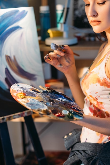 Pintura hobby Arte pasión Pintor estilo de vida Inspirado artista femenina pensativa con pincel paleta colorida obra de arte abstracta en caballete en taller creativo
