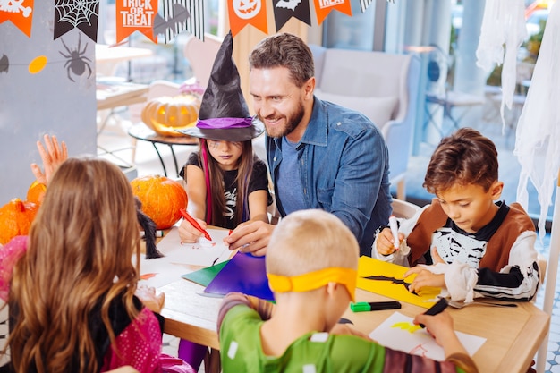 Pintura de murciélagos. Sonriente padre barbudo guapo ayudando a sus hijos a pintar murciélagos y arañas para Halloween