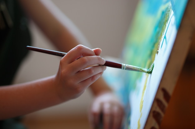 Pintura de niña preescolar en clase de arte. Ciérrese encima del cepillo de la foto en la mano.