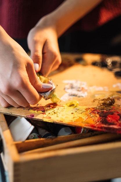 Pintura profissional Ferramentas de artista Passatempo criativo Mãos de pintora feminina aplicando tinta acrílica de tubo usado na velha paleta de madeira suja vintage