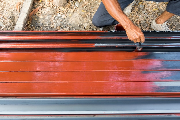 Una pintura del trabajador a prueba de herrumbre en los postes de acero para la construcción.