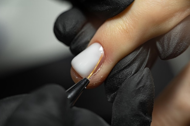 Pintura para uñas de manicura con pincel fino en el salón de belleza Manos de la manicurista de cerca Esmalte de uñas de artista