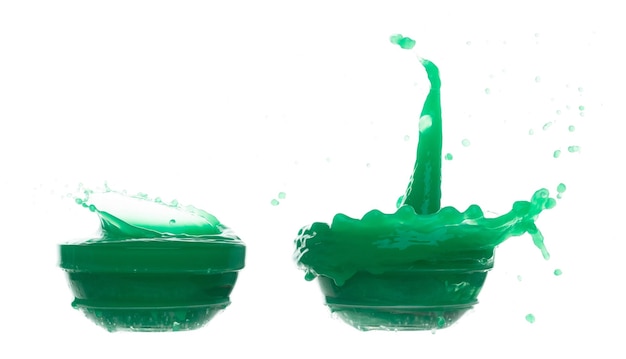La pintura verde líquida vuela en el aire derramando tazón de vidrio zumo de manzana y verdura cayendo dispersos