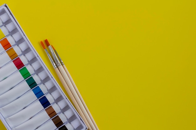 Pinturas acrílicas brillantes en tubos y pinceles para dibujar sobre un fondo amarillo