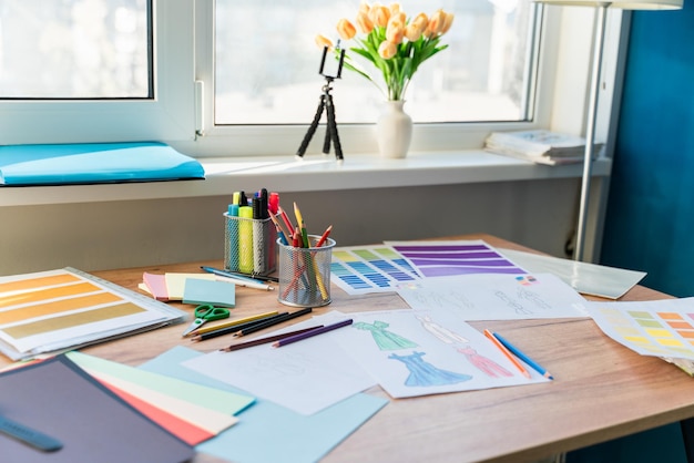 Pinturas, lápices de colores y bocetos de vestidos creativos inusuales colocados en la mesa. Lugar de trabajo del concepto de diseñadora de vestuario de una mujer