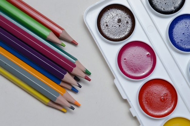 Pinturas multicolores para dibujar en paleta, pincel y lápices sobre un fondo claro. de cerca.