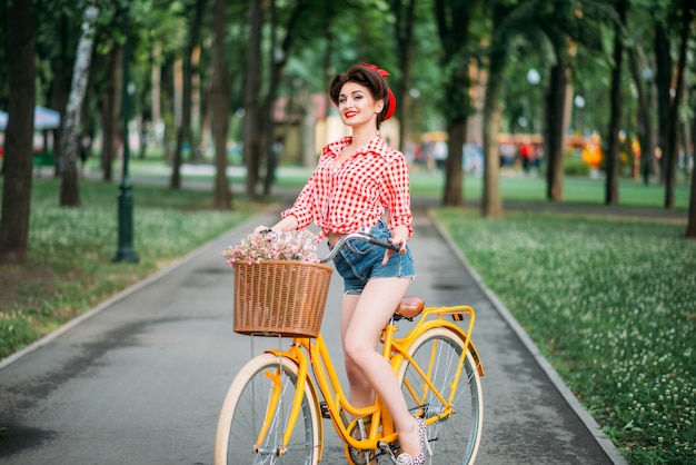 Pinup-Mädchen auf Retro-Fahrrad mit Blumenrücken