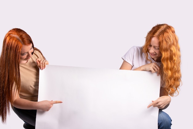 Pinup mujeres mostrando las manos del dedo índice en la foto de banner en blanco para el conjunto de anuncios de jóvenes modelos caucásicos pinup pelirrojos sobre fondo gris con espacio para texto