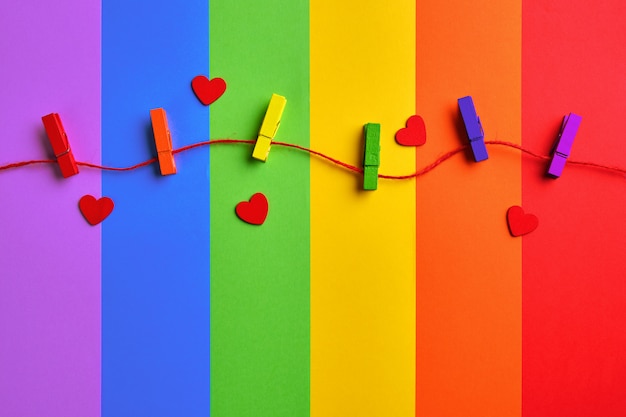 Pinzas de madera de colores del arco iris y corazones rojos sobre fondo de bandera del arco iris