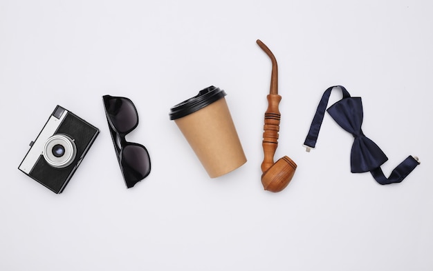 Pipa y pajarita, gafas de sol y cámara, taza de café sobre fondo blanco. Complementos de caballero. Vista superior