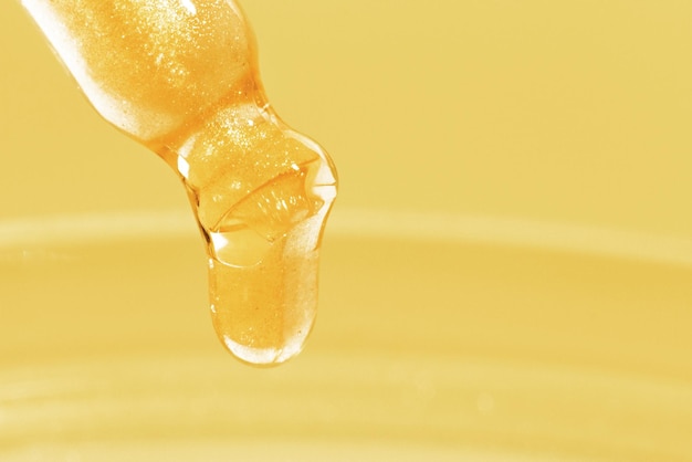 Pipeta com líquido amarelo pingando ou ouro líquido Detalhe sobre um fundo dourado Medicina química de laboratório Brilho de pesquisa cosmética