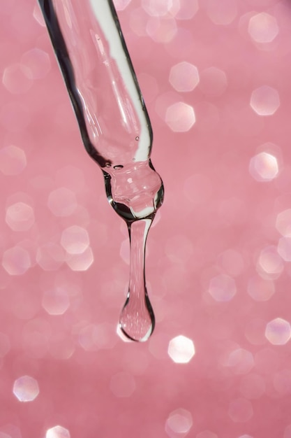 Pipeta cosmética com uma gota em fundo rosa