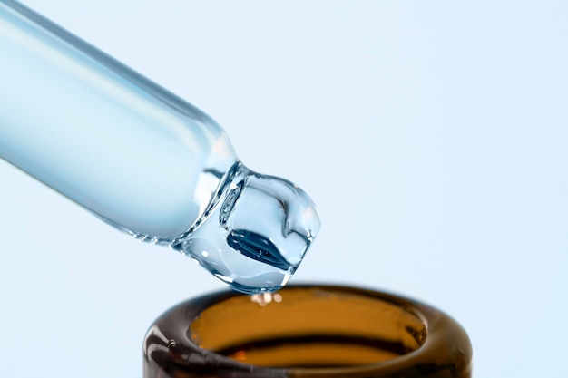 Pipeta de vidro cosmético com óleo de soro transparente e garrafa marrom sobre fundo azul Beleza