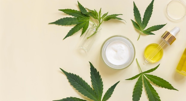 Pipeta e frasco de creme aberto perto de cannabis verde deixa visão superior em cosméticos CBD bege