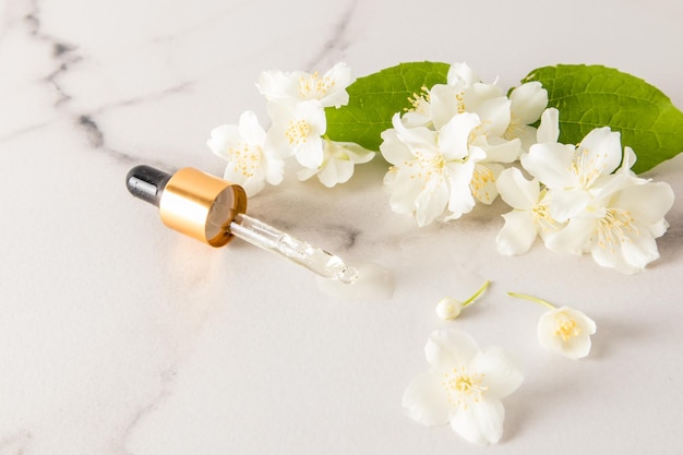 Una pipeta llena de aceite de jazmín natural se encuentra sobre una mesa blanca de mármol con flores aromáticas, una copia del espacio