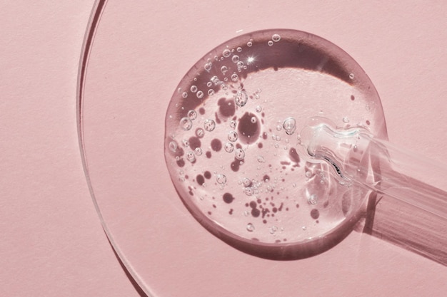Pipeta con muestra de producto cosmético geles en placa de petri sobre sombras duras de fondo rosa