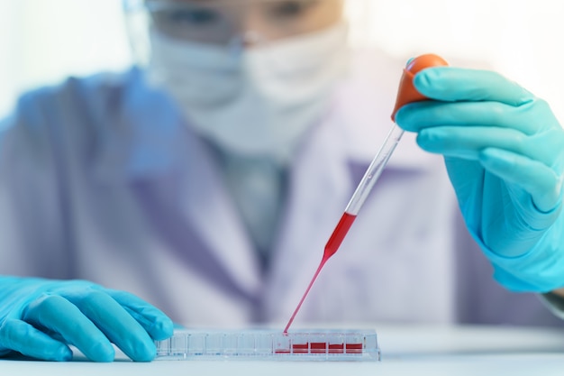 Pipetar adicionando fluido aos tubos de ensaio. Assistente de laboratório, analisando uma amostra de sangue.
