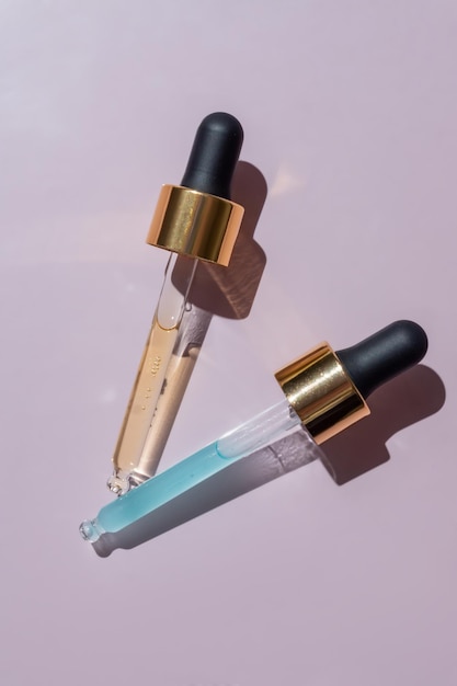 Pipetas transparentes com soro de cosméticos azul e amarelo em um fundo rosa claro Textura do produto Maquete de marca de garrafa de vidro conta-gotas Pipeta cosmética