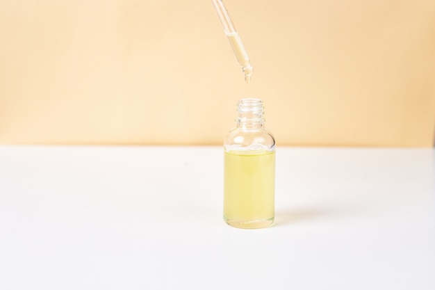 Pipette mit ätherischem Öl über Flasche auf weißem und gelbem Hintergrund. Konzept der Naturheilkunde. Aromatherapie