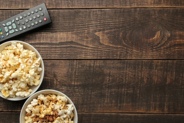 Pipoca e controle remoto de TV em uma mesa de madeira marrom, conceito de assistir filmes em casa, vista de cima