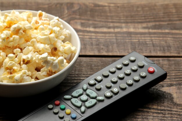 Pipoca e controle remoto de TV em uma mesa de madeira marrom, o conceito de assistir filmes em casa.