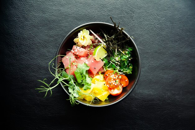 Pique a salada com atum em uma tigela. Ingredientes atum fresco, tomate cereja, alga marinada, arroz, takuan, molho Ponzu, molho Teriyaki, nori, sementes de gergelim, limão, coentro. Conceito de salada de frutos do mar asiáticos.