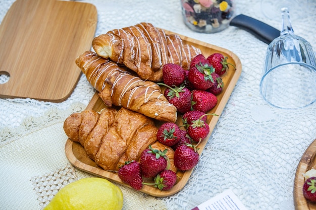 Piquenique ao ar livre em um parque verde exuberante com um saboroso croissant, rosquinhas de frutas e vinho na grama